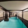 Indoor luxury hotel pool with black pillars and white-paneled walls, seating area visible at far end.