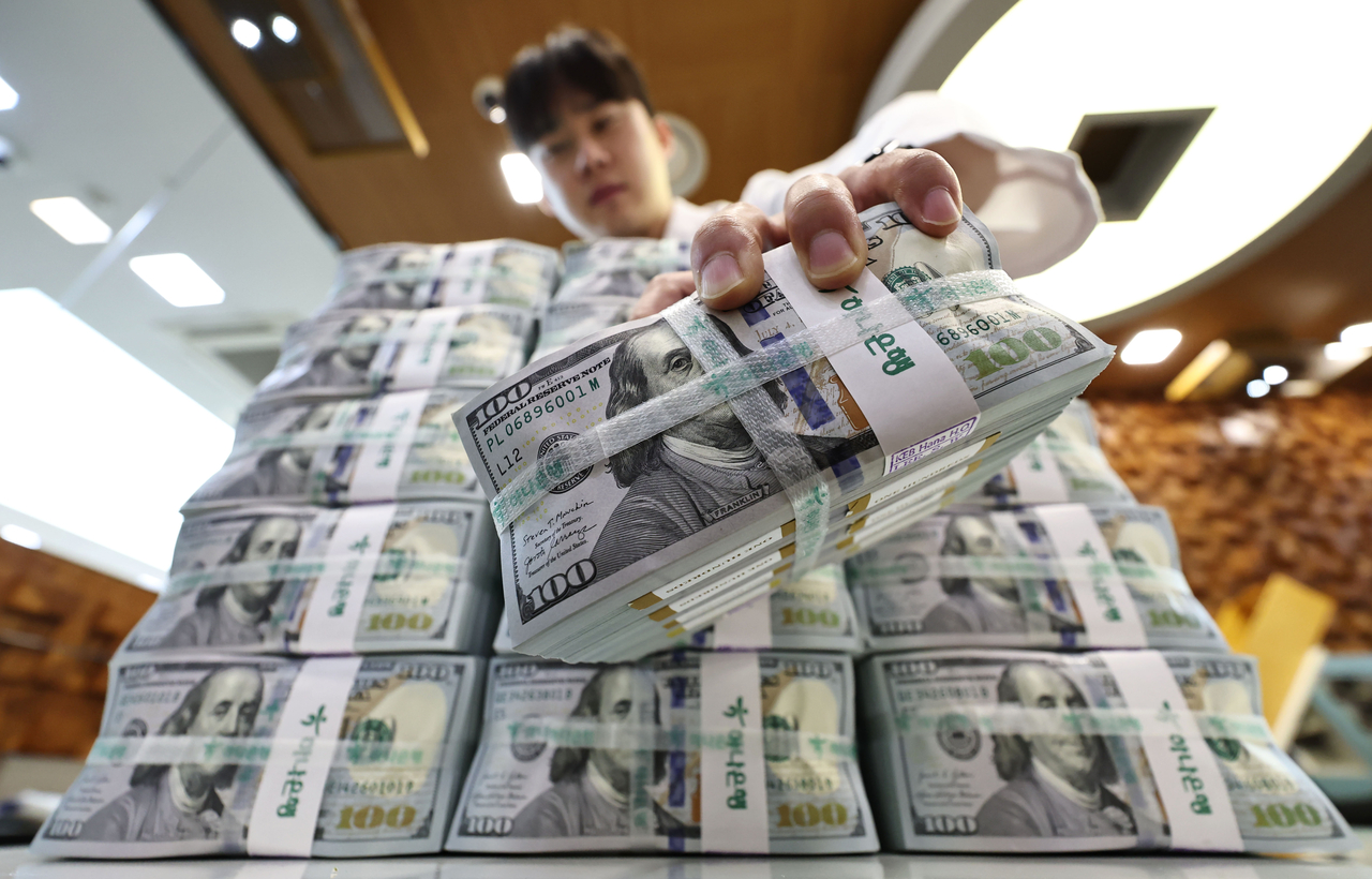 An employee at Hana Bank holds up a bundle of US dollars on Thursday. (Yonhap)